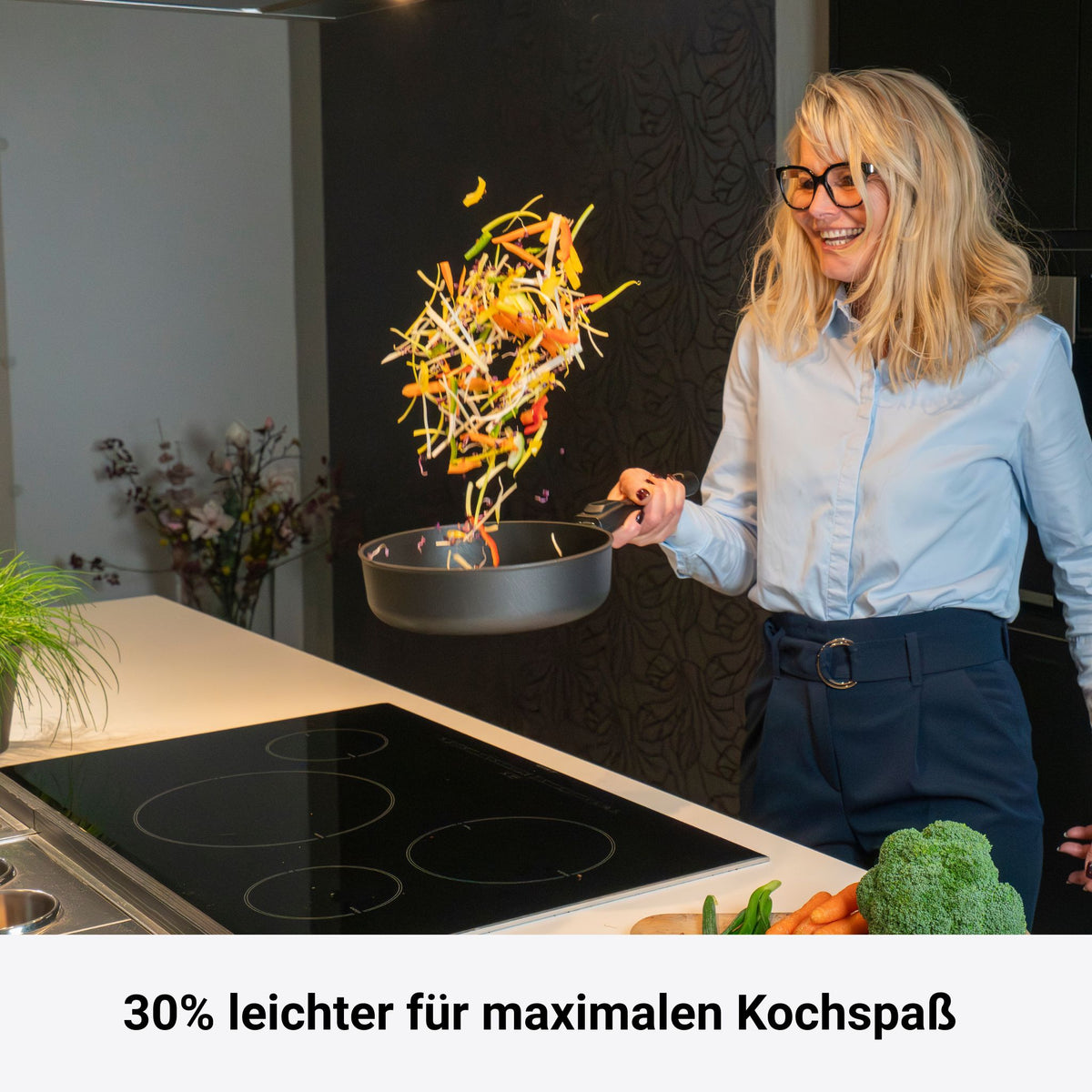 Schwarze Viereckpfanne mit Holzgriff, Gemüse wird in der Luft geworfen.
