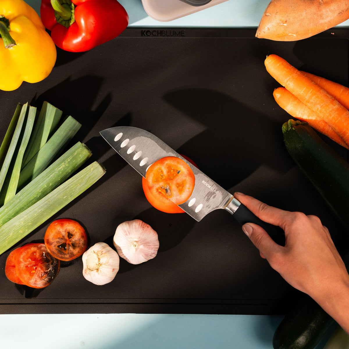 XL schwarze Schneidunterlage mit Gemüse und Hand, die Tomate mit scharfem Messer schneidet.