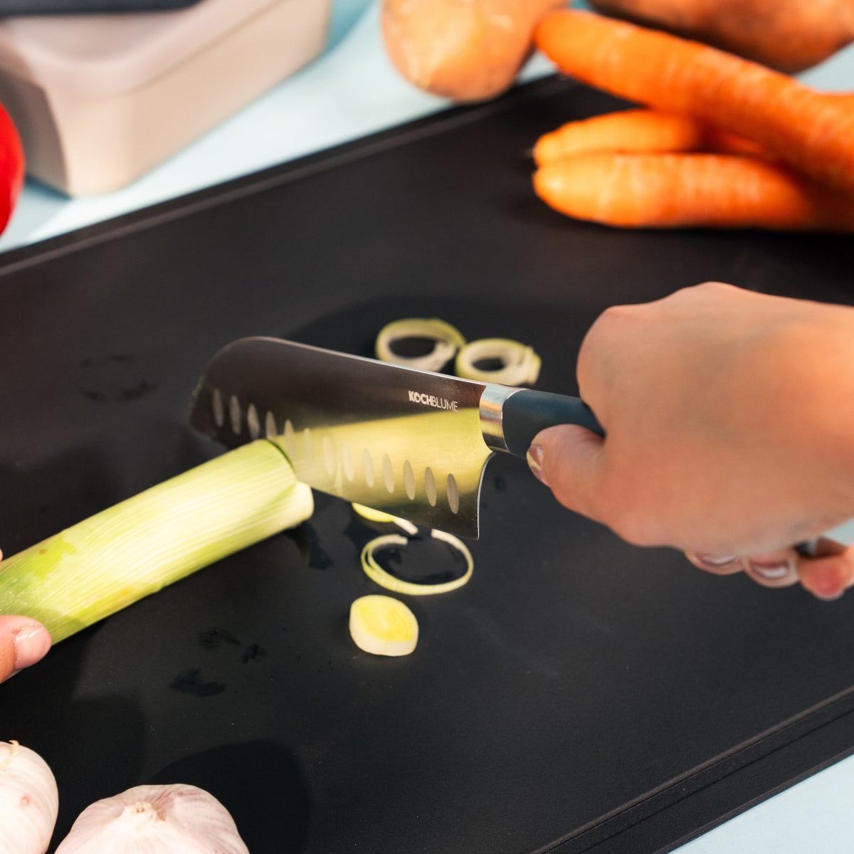 Schwarze Schneidunterlage mit geschnittenem Lauch und Karotten im Hintergrund.