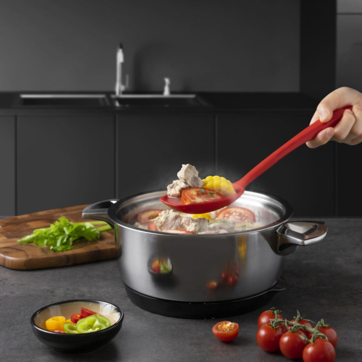 Soßenlöffel in Rot aus Kunststoff, der Suppe aus Edelstahltopf schöpft.