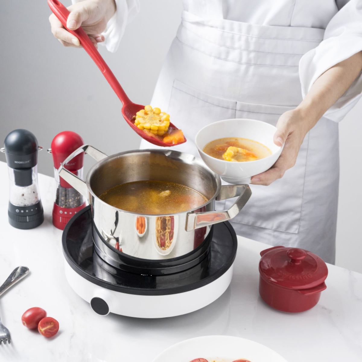 Roter Soßenlöffel aus Kunststoff mit langem Griff entnimmt Suppe aus Edelstahltopf auf Herdplatte.