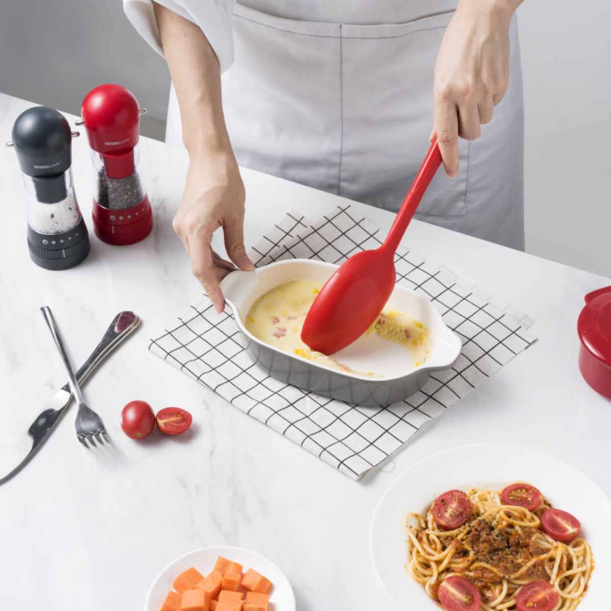 Roter Soßenlöffel mit langem Griff aus flexiblem Material in kleiner grauer Pfanne.