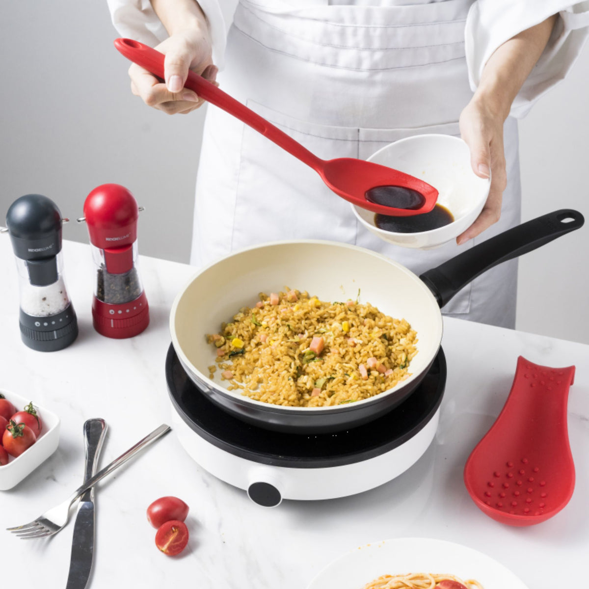 Roter Soßenlöffel aus Silikon, der Reis aus Pfanne auf weißen Teller gibt.