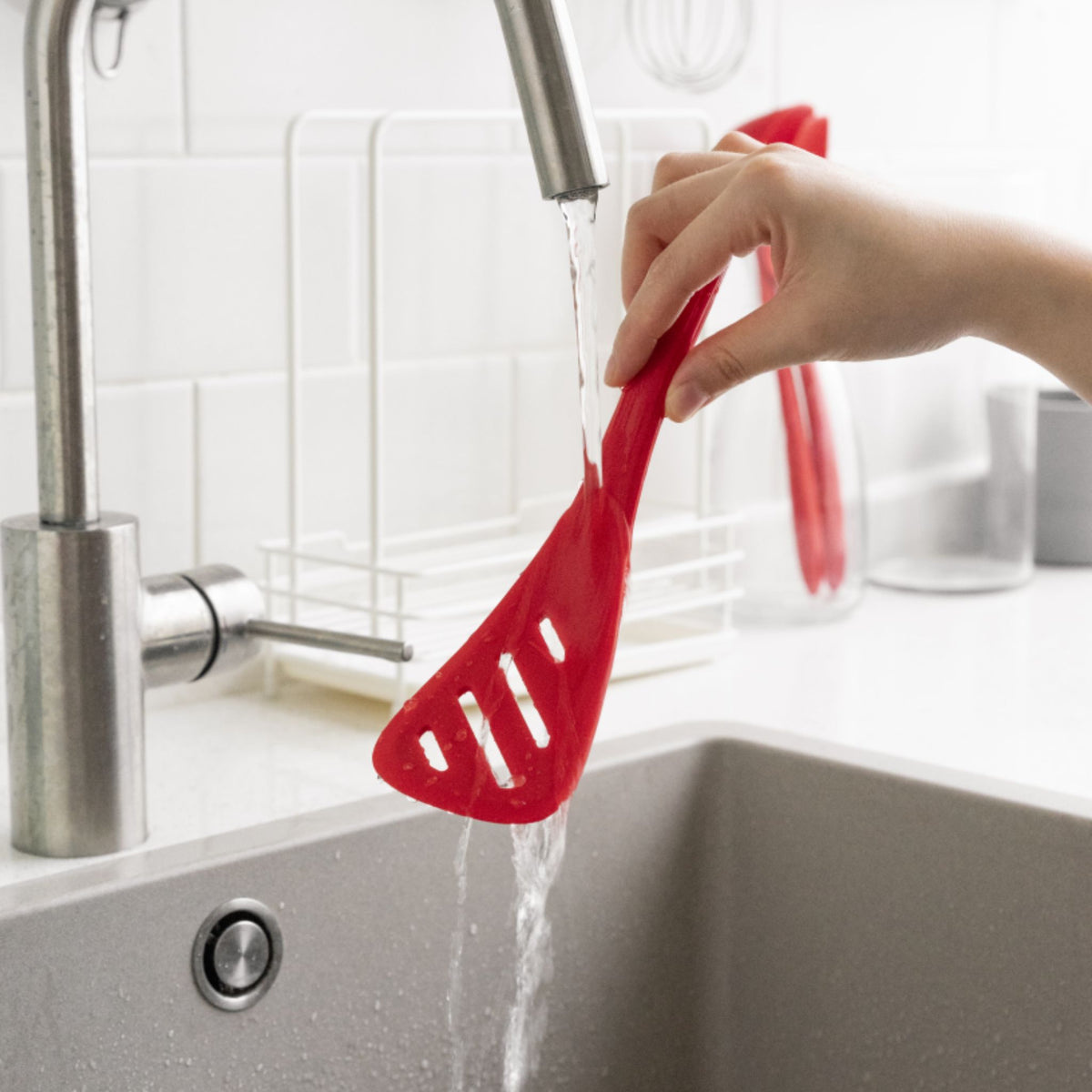 Roter Schlitzwender aus Kunststoff, der unter fließendem Wasser gehalten wird.