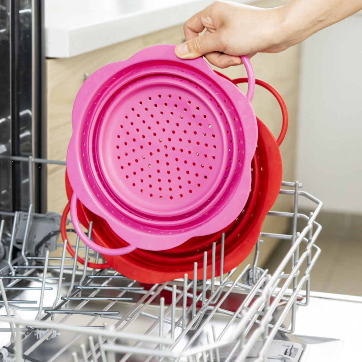Faltbares Abtropfsieb in Pink aus flexiblem Silikon mit Griffen in Geschirrspüler eingesetzt.