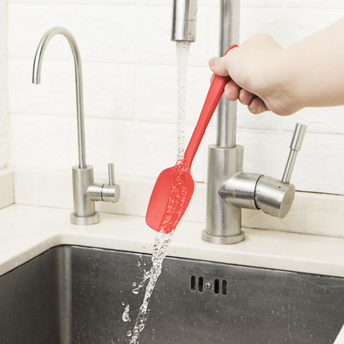 Roter Flexlöffel mit langem Griff unter fließendem Wasser am Spülbecken.