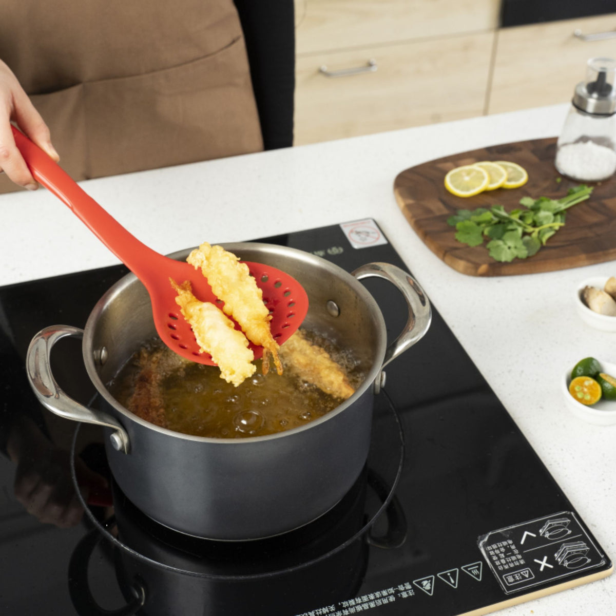 Roter Schaumlöffel hebt paniertes Essen aus kochendem Öl in grauem Topf hervor.