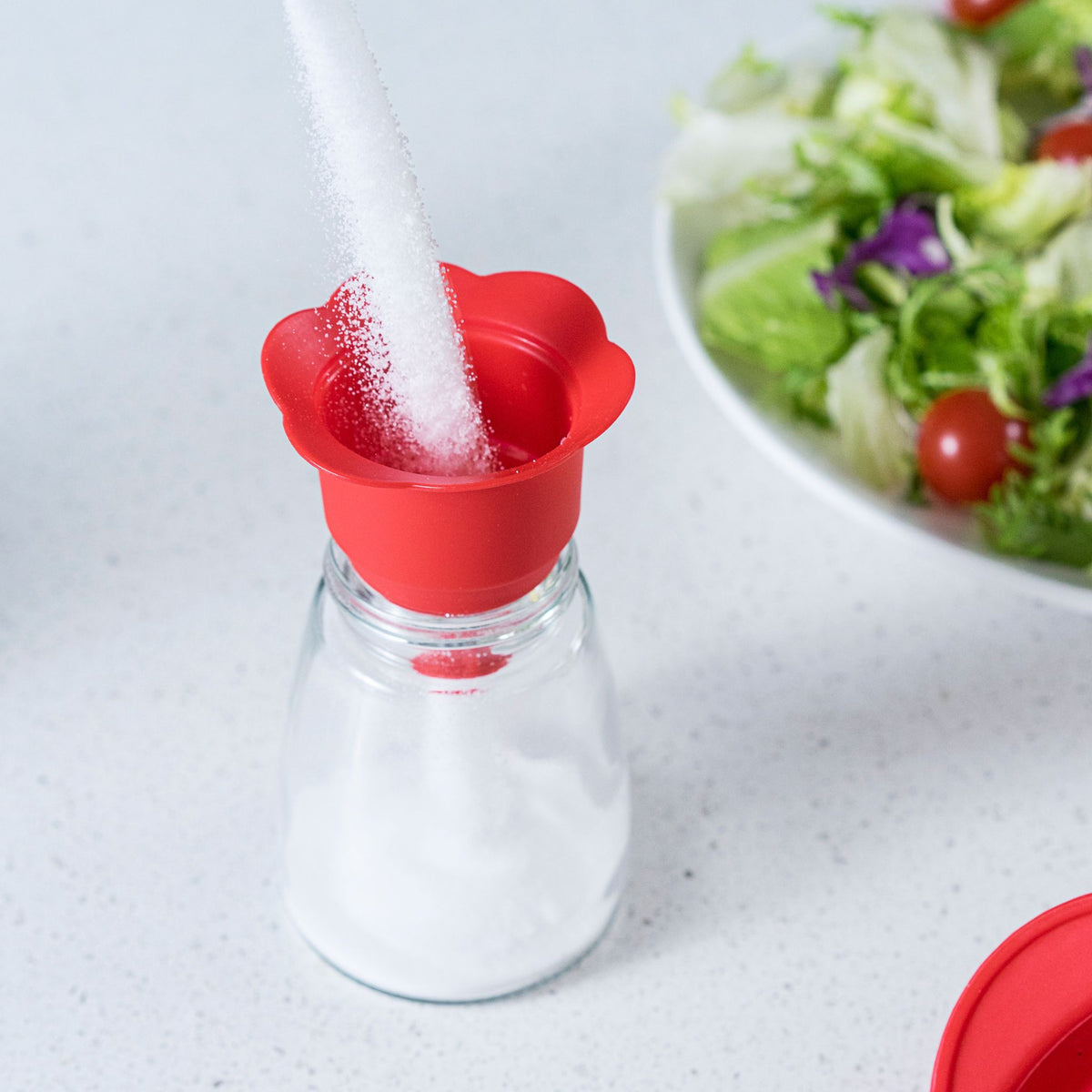 Roter Falttrichter aus Silikon mit blütenförmiger Öffnung auf Glasflasche.