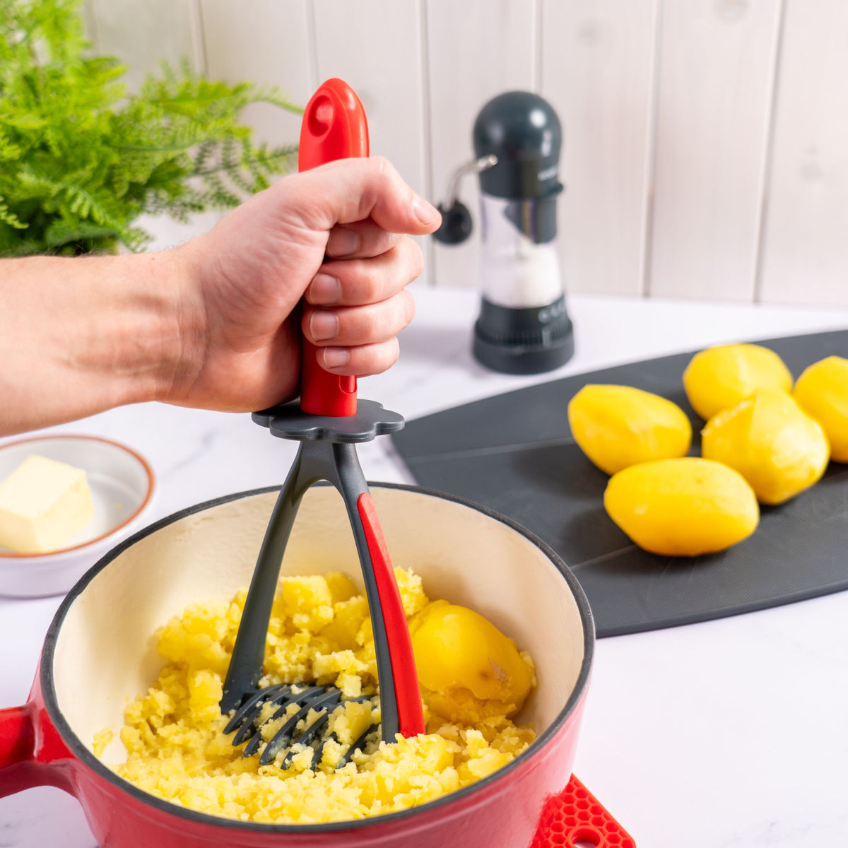 Roter Kartoffelstampfer aus Kunststoff und Metall in einem Topf mit gekochten Kartoffeln.