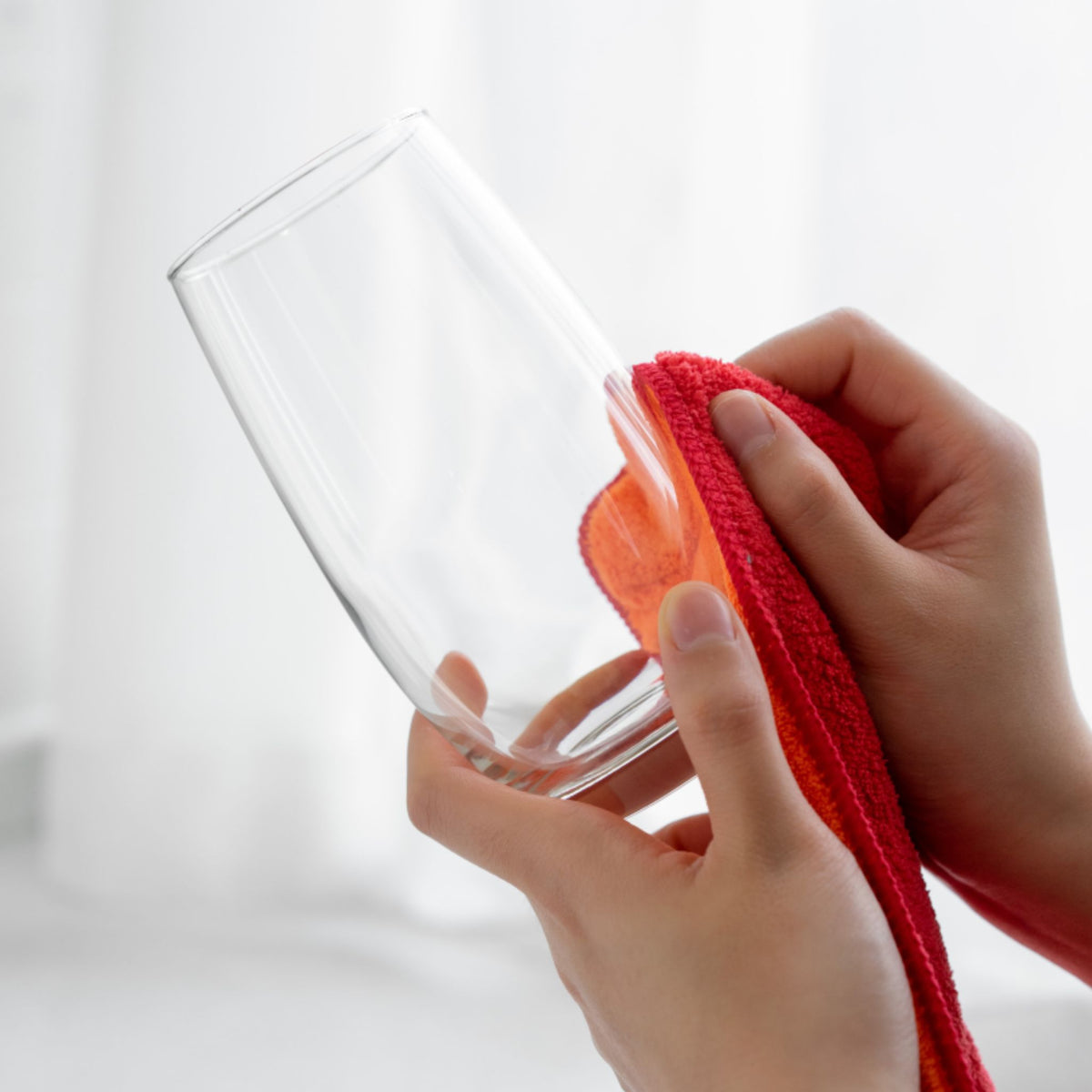 Hände reinigen klares Glas mit rotem Mikrofaser-Tuch.