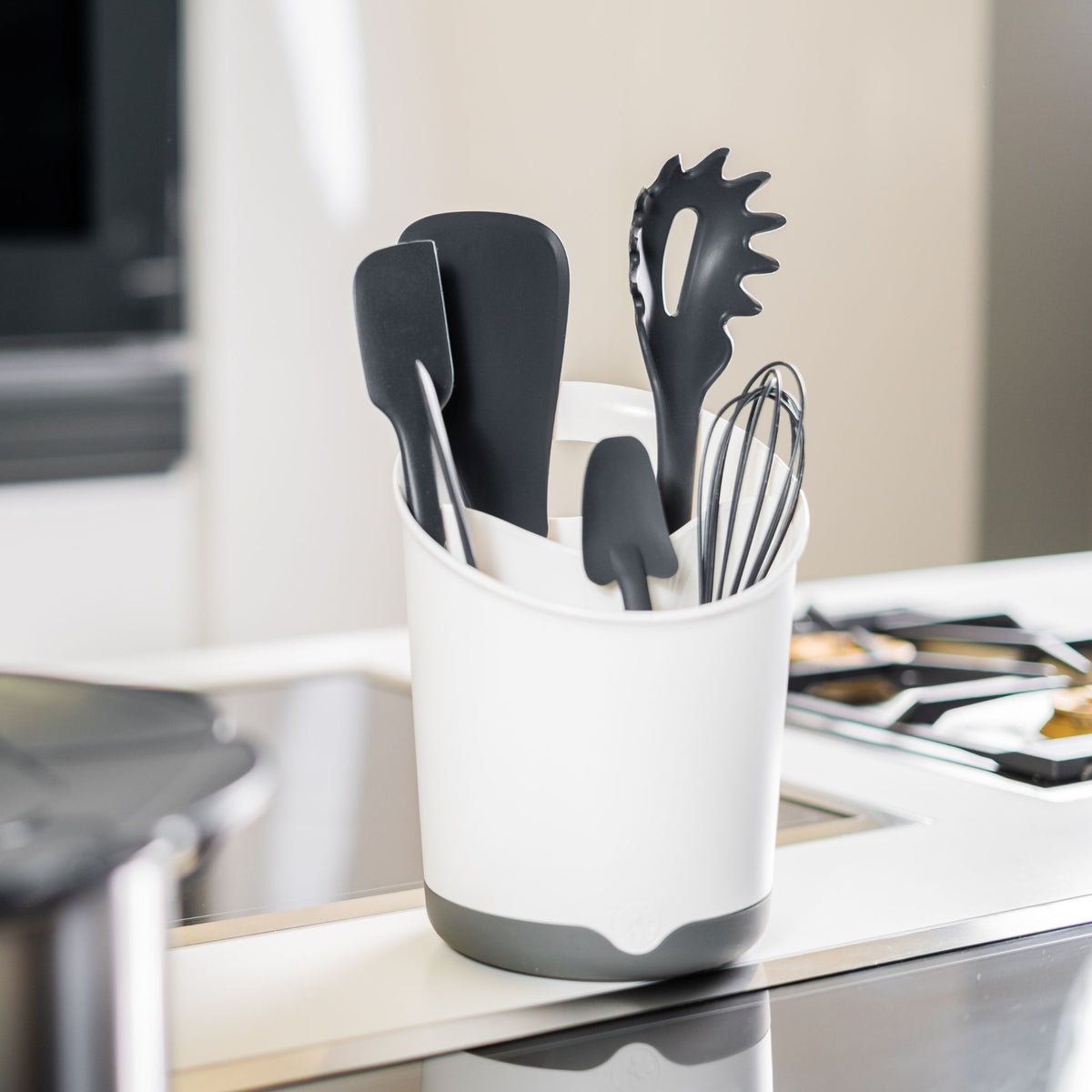 Weißer Utensilienbehälter mit grauem Boden, gefüllt mit schwarzen Küchenhelfern aus Kunststoff und Metall.
