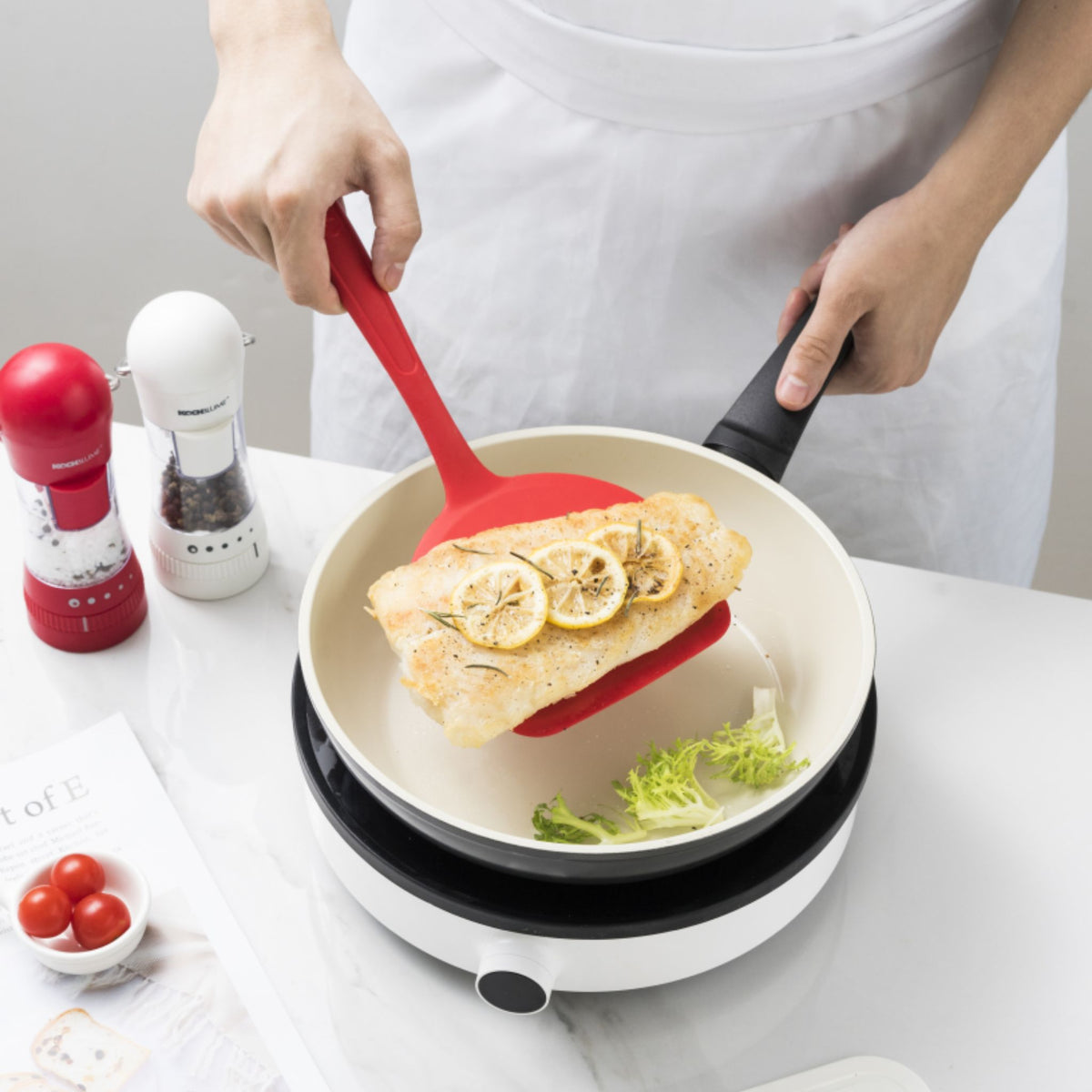 Roter Fischwender aus Kunststoff beim Anheben gebratener Fischfilets aus einer Pfanne.