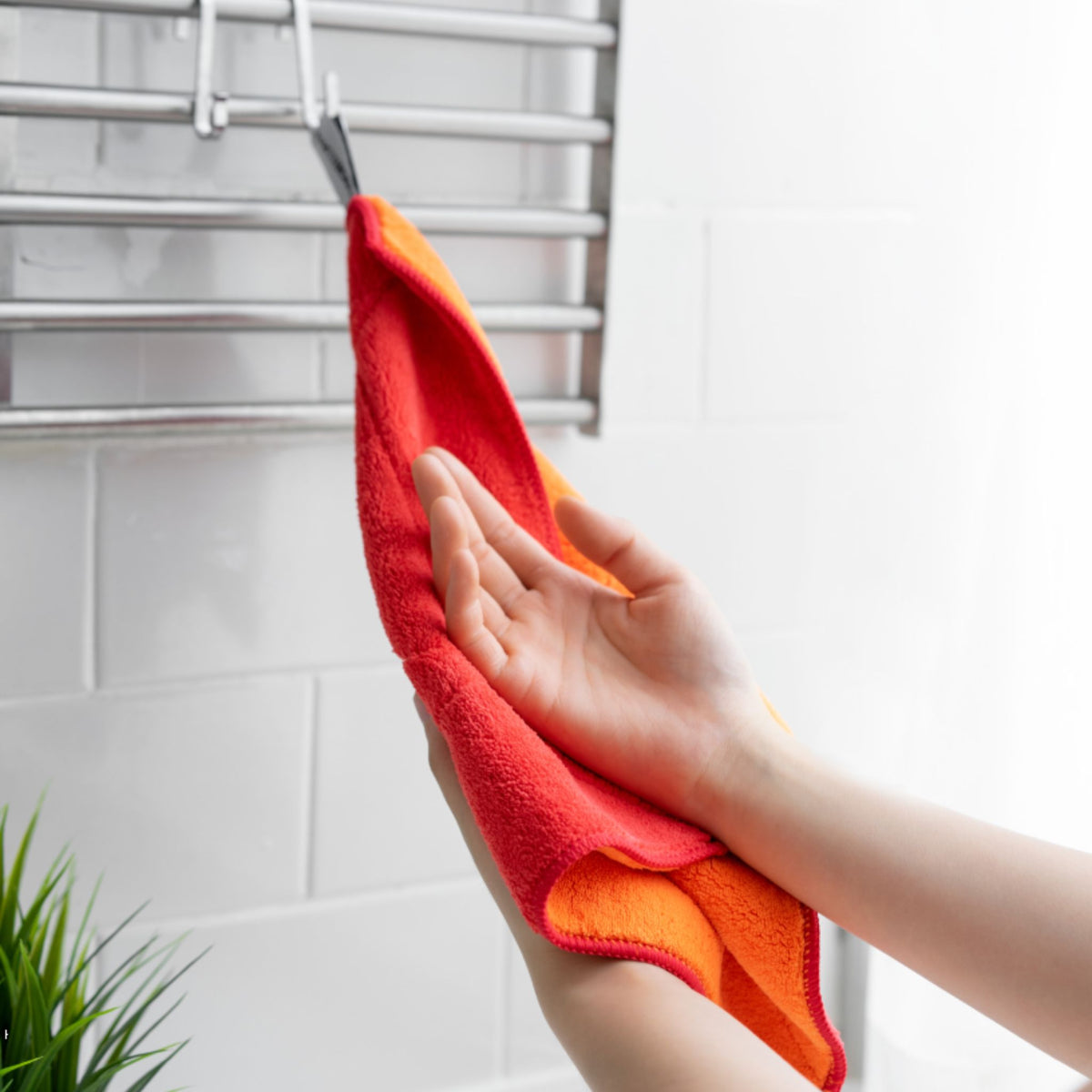 Rotes und orangefarbenes Geschirrtuch aus weichem Stoff in Hand, hängend an Metallgitter.