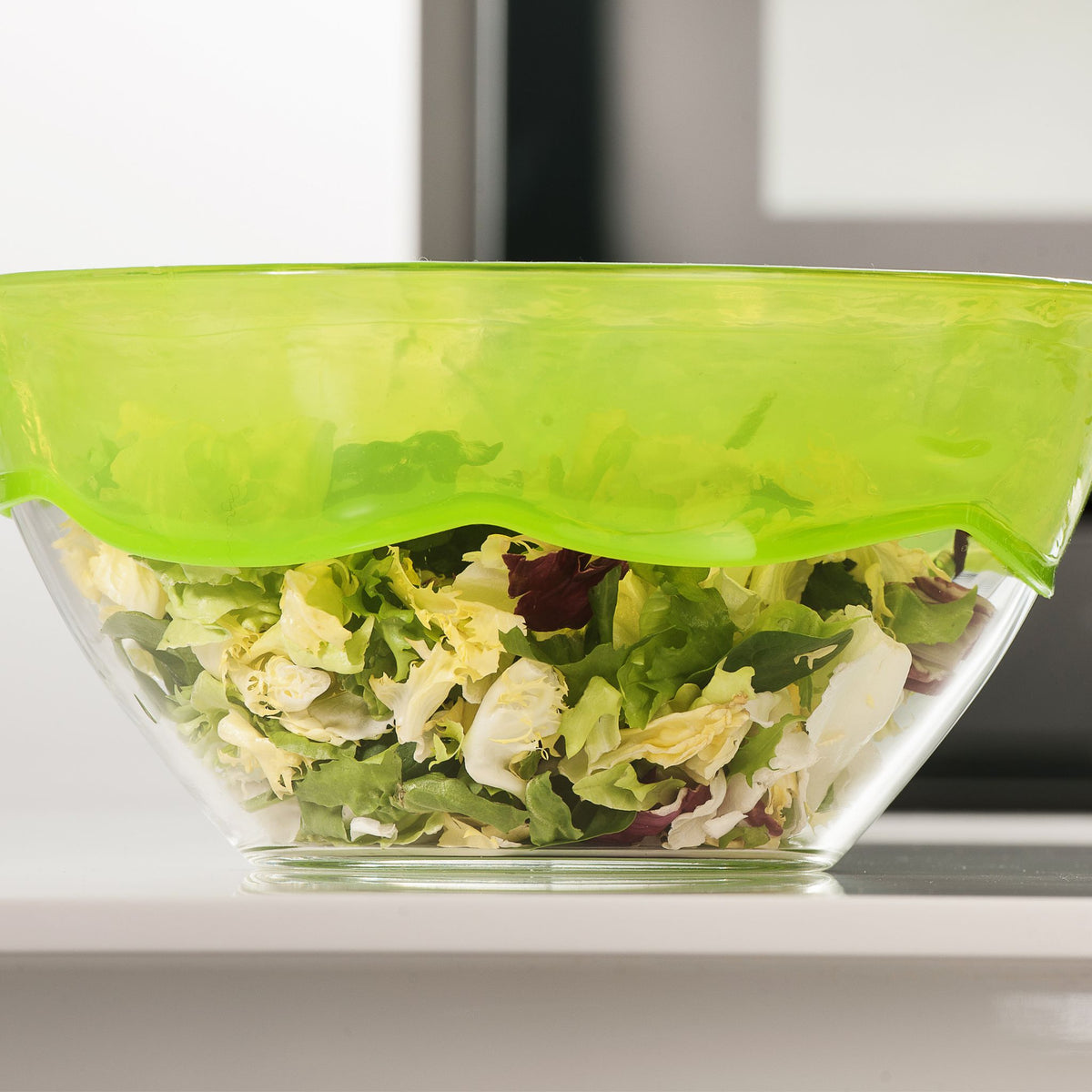 Glas-Schüssel mit grünem Stretch-Deckel, gefüllt mit gemischtem Salat.