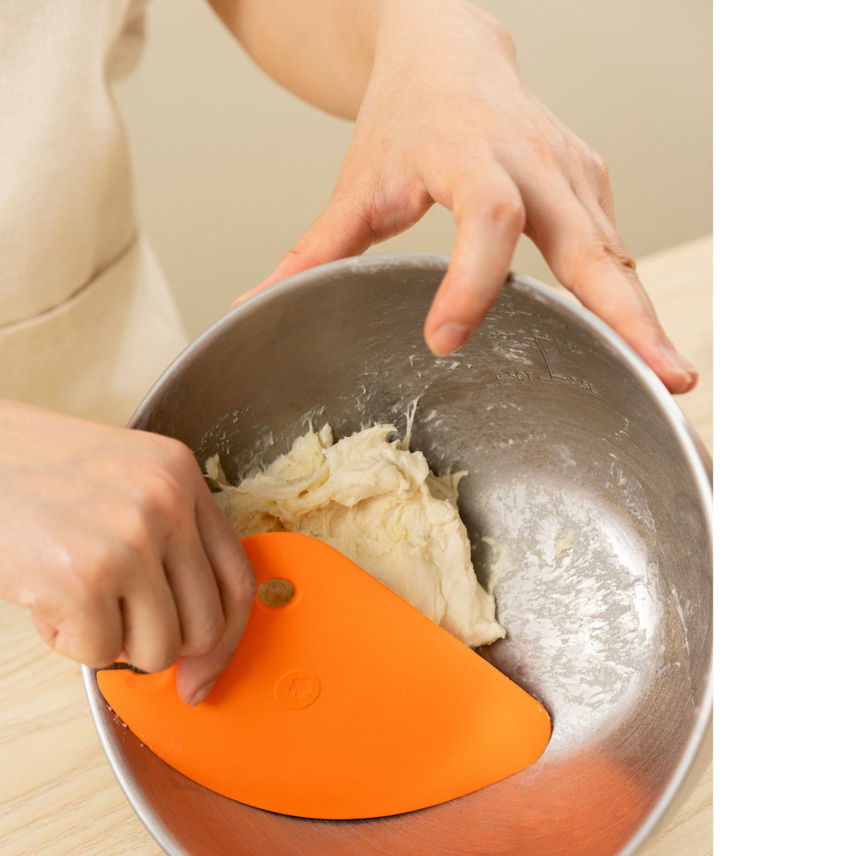 Hand hält orangefarbene Teigkarte in Edelstahlschüssel mit Teig.