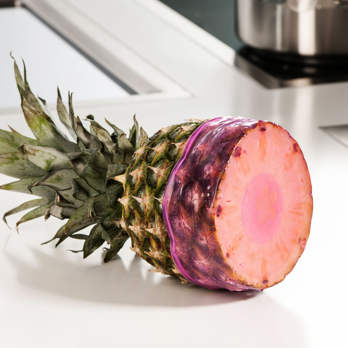Aufgeschnittene Ananas mit grünem Blattkranz liegt auf weißer Oberfläche.