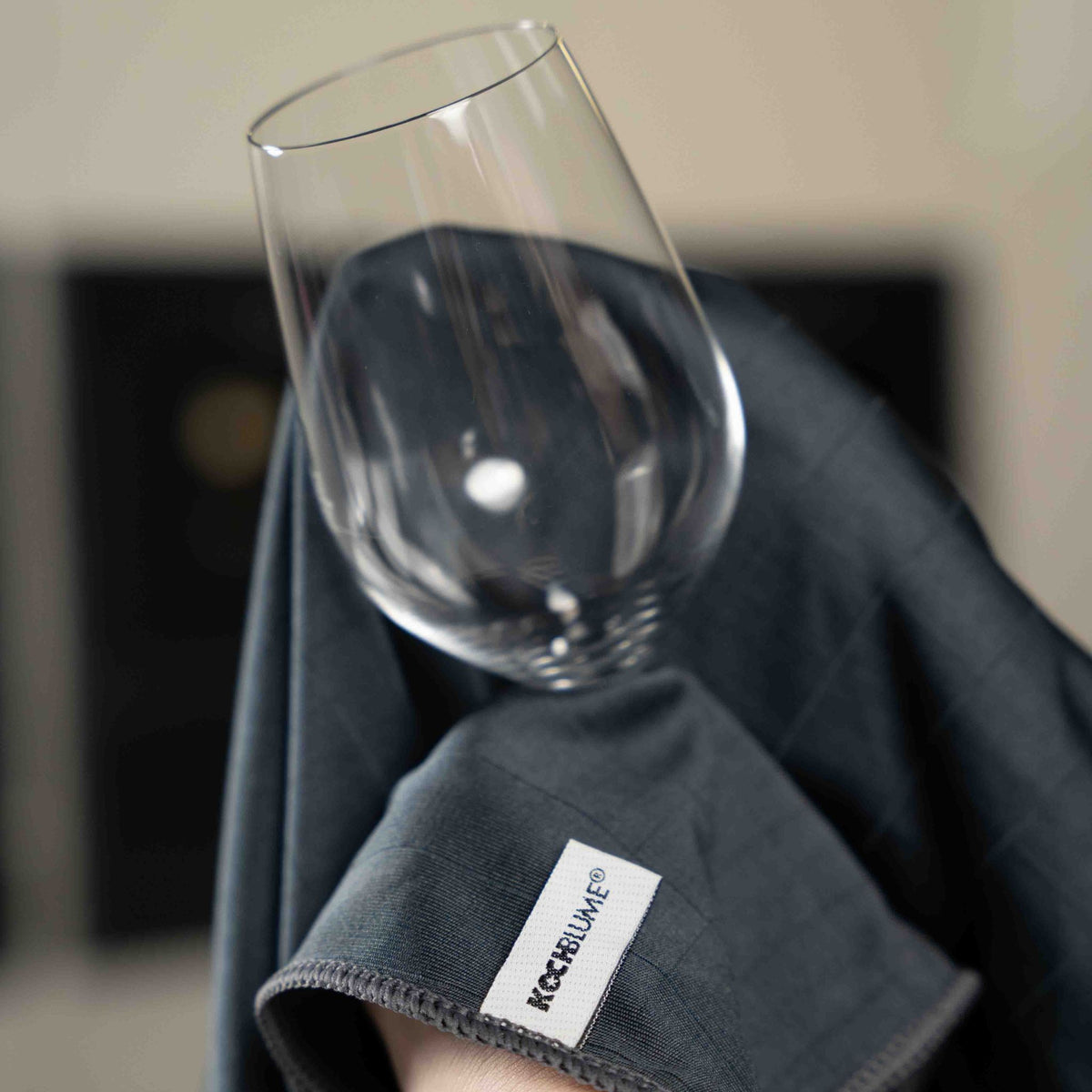 Anthrazitfarbenes Poliertuch mit Label, Glas zum Polieren darauf gestellt.