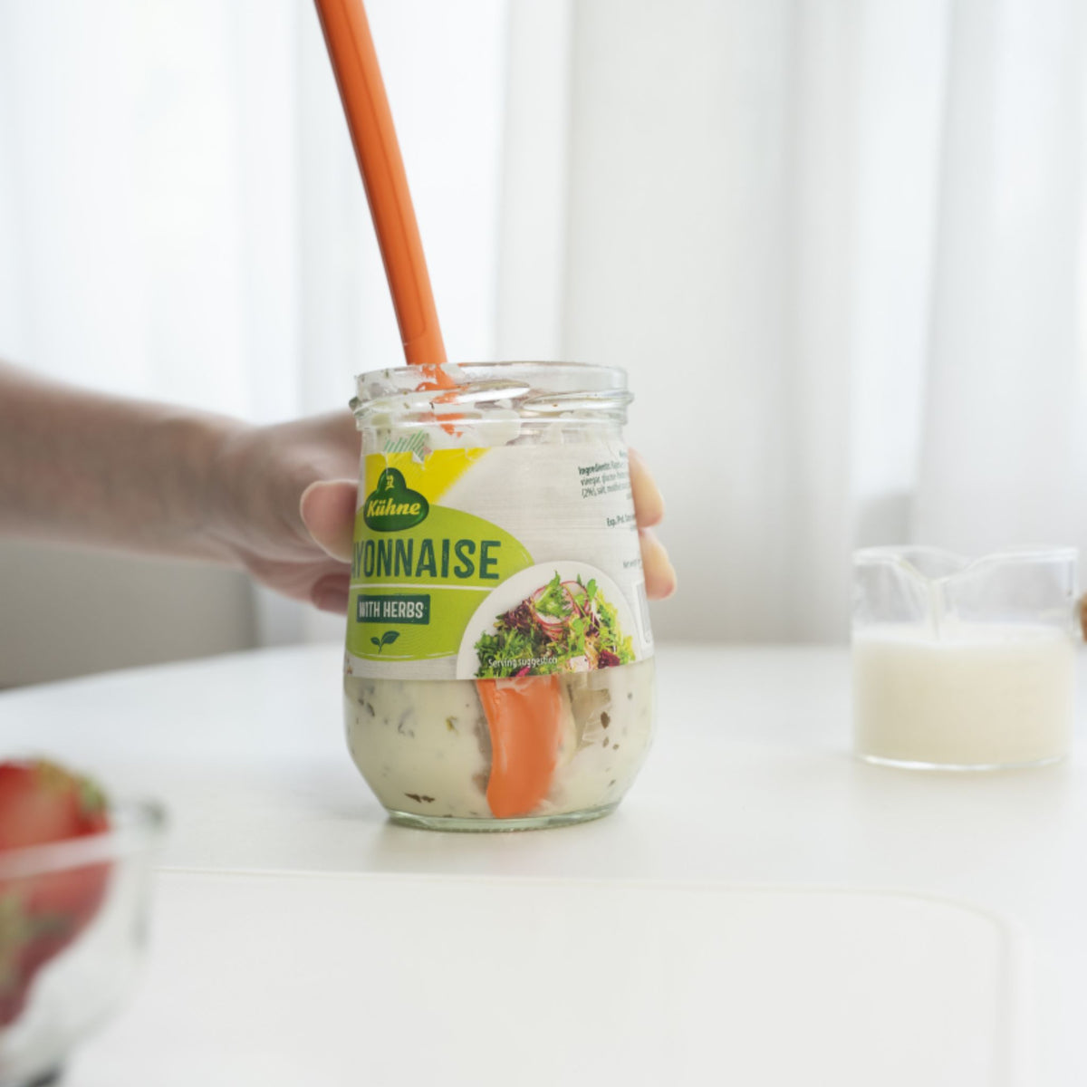 Anthrazitfarbener Restelöffel in einem Glas mit Mayonnaise auf weißer Arbeitsfläche.