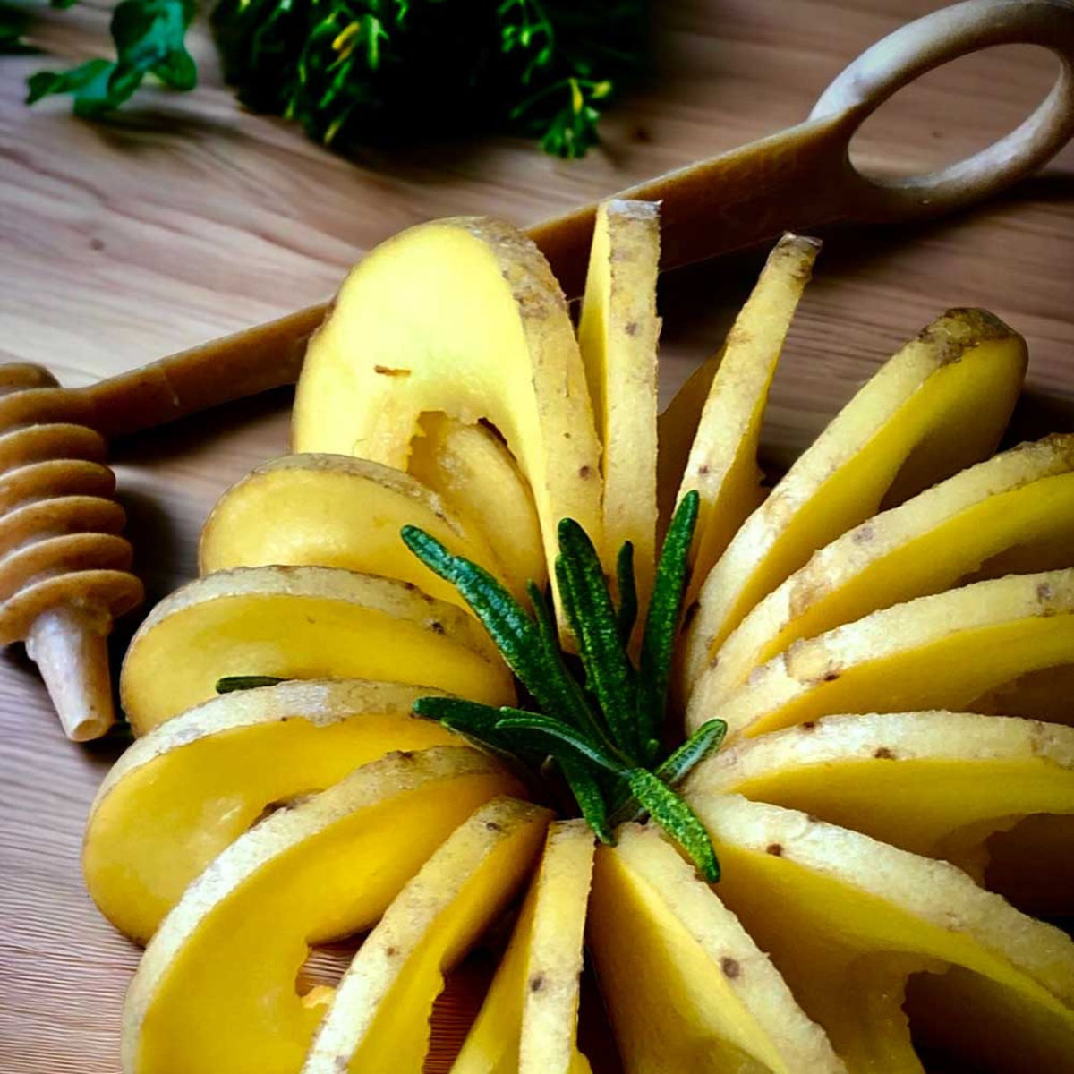 Spiralschneider mit dünn geschnittenen Kartoffelscheiben und Rosmarinzweig auf Holzbrett.