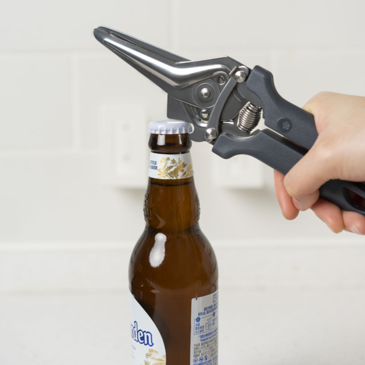 Anthrazitfarbene Küchenschere mit Flaschenöffner-Funktion, in Aktion über einer Bierflasche.