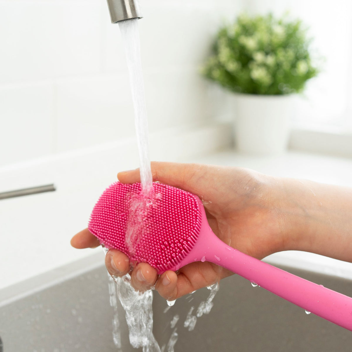 Spülbürste in Pink mit weichen Silikonborsten unter fließendem Wasser in Hand gehalten.