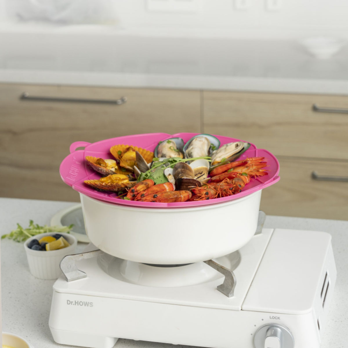 Weißer Kochtopf mit rosa Silikondeckel und Meeresfrüchten als Inhalt auf Gasherd.