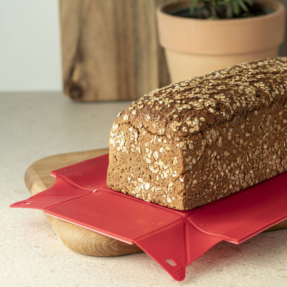 Rote flexible Silikon-Backmatte unter Vollkornbrot auf Holzbrett.