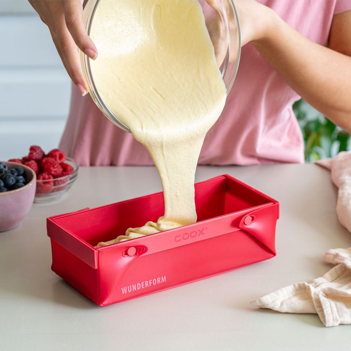 Rote, rechteckige Silikonbackform mit hineingegossenem Teig und abnehmbarem Griff.