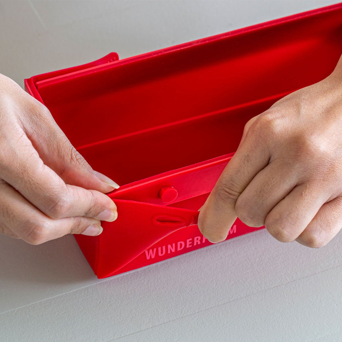 Rote, faltbare Silikonform mit glatter Oberfläche und Handschuhen zum Zusammenfalten.