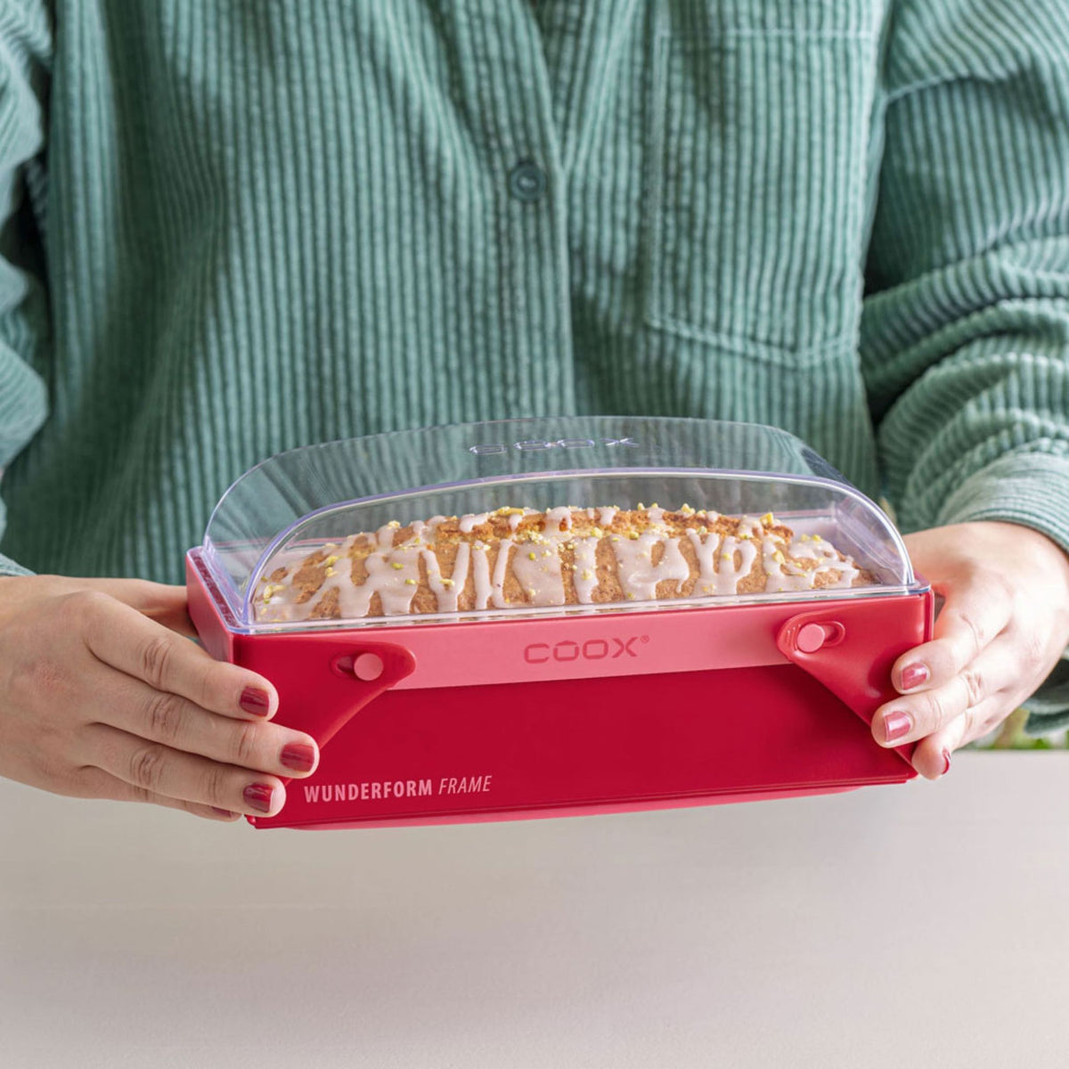 Rechteckige Coox-Wunderform L Backform mit Glasdeckel und roten Silikongriffen, gefüllt mit Kuchen.
