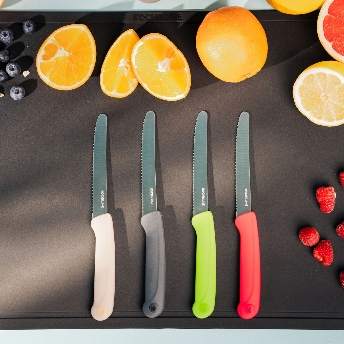 Vier Frühstücksmesser mit wellenschliff Klingen und bunten Griffen in Beige, Anthrazit, Limette und Rot auf schwarzem.