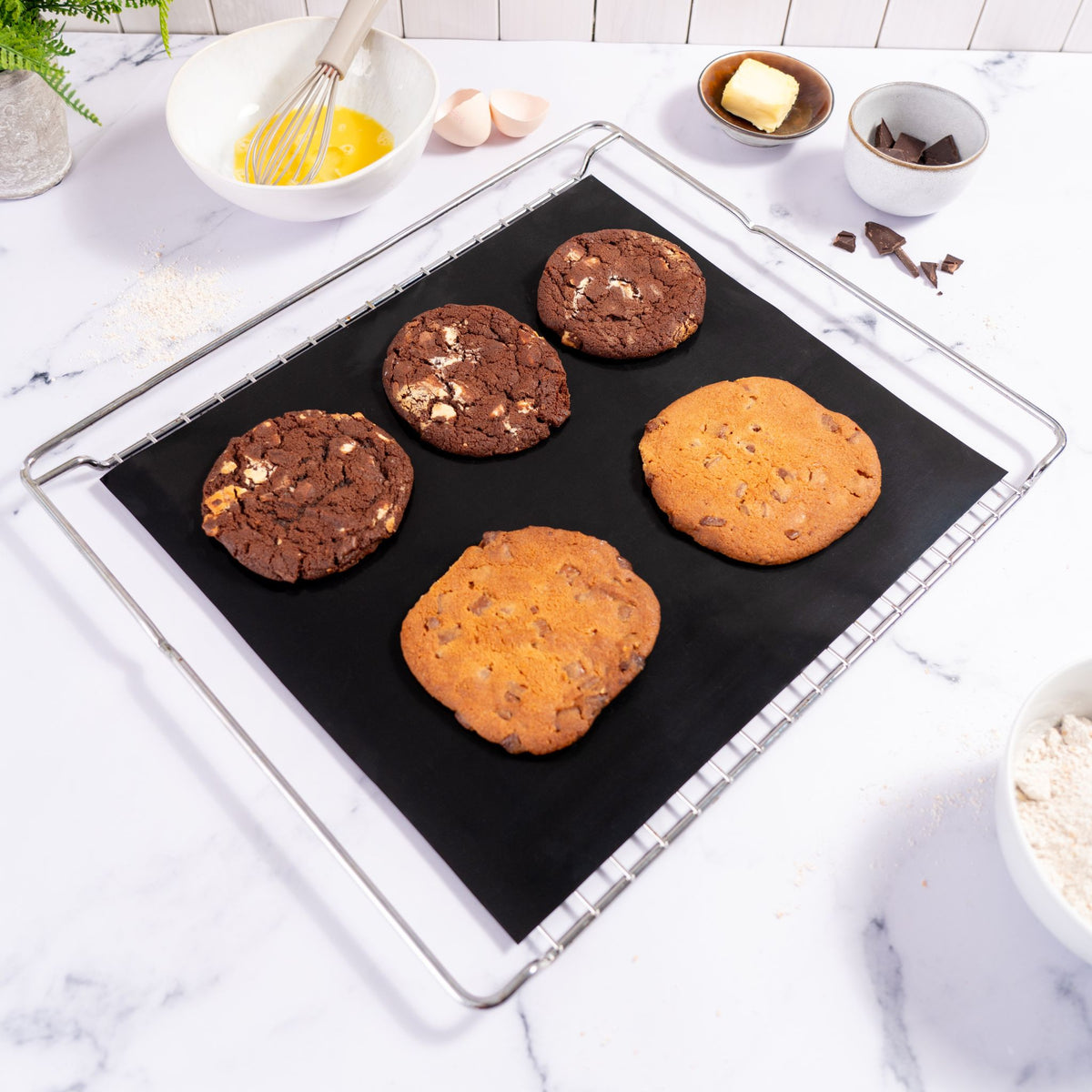 Backblech mit schwarzer Dauerbackfolie und vier frisch gebackenen Cookies darauf.
