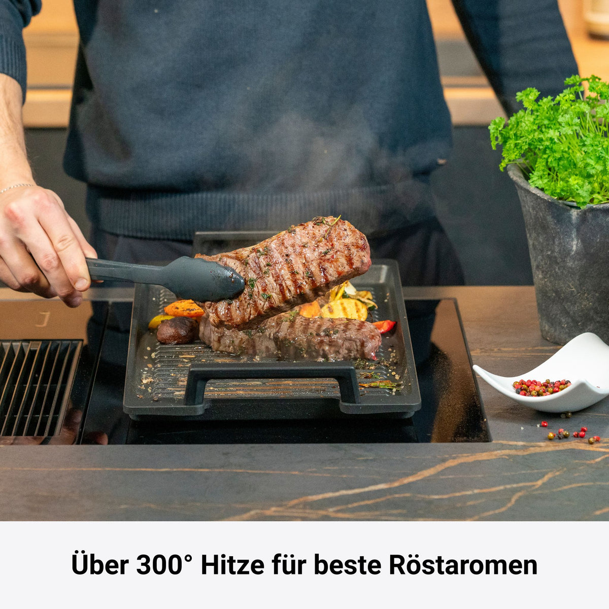 Pfanne mit Grillrost aus Gusseisen und klappbarem Griff, braunes Grillgut darauf.