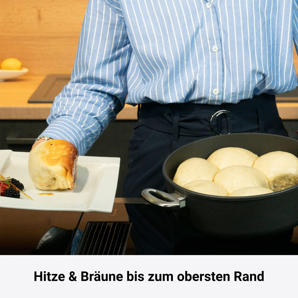 Schwarze Viereckpfanne mit Edelstahlgriff, gefüllt mit Teigbällen, auf Kochfeld mit Person im Hintergrund.