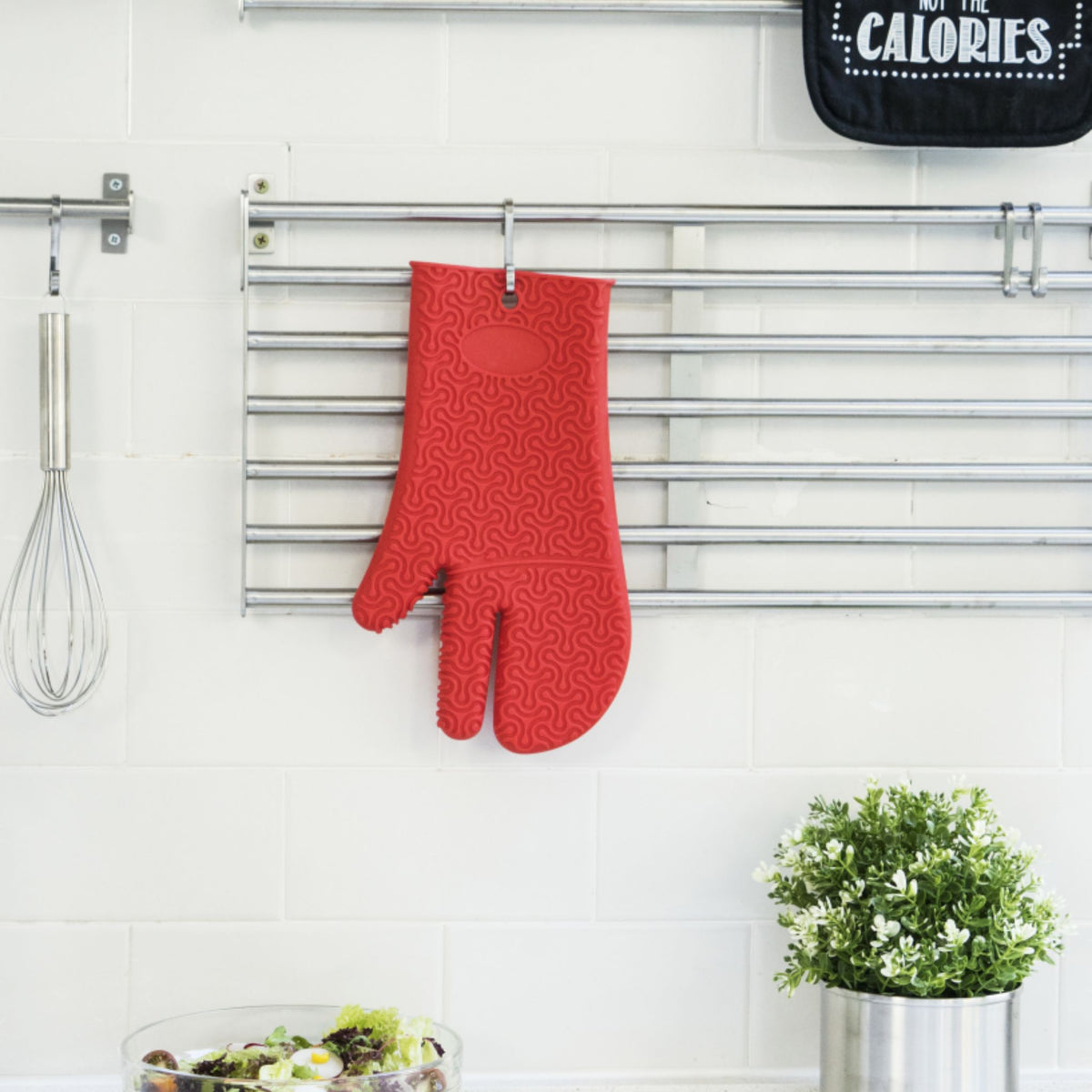 Roter Ofenhandschuh mit Textur, hängend an einer Küchenleiste vor weißer Wand.