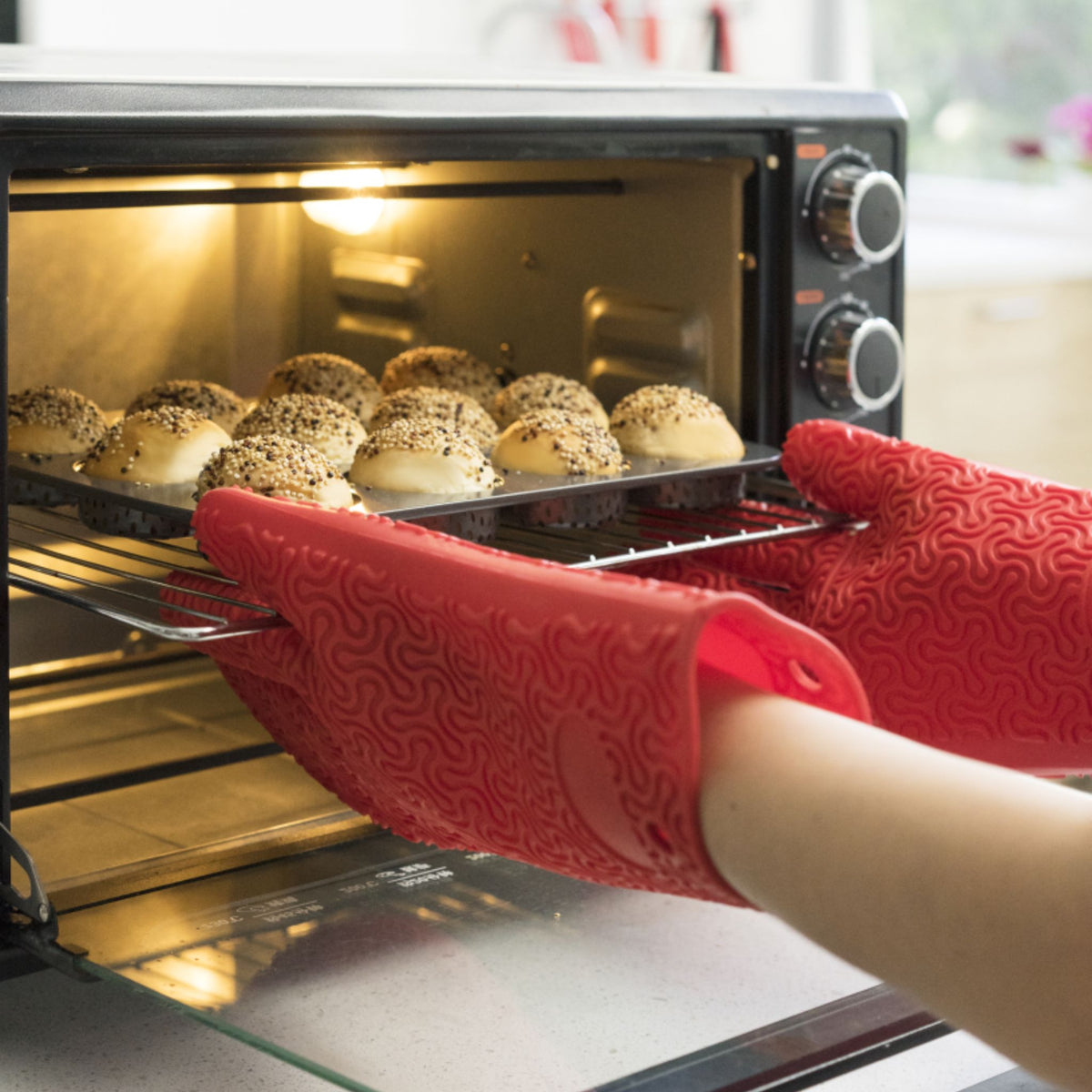 Rote Ofenhandschuhe greifen Backblech mit frisch gebackenen Brötchen aus dem Ofen.
