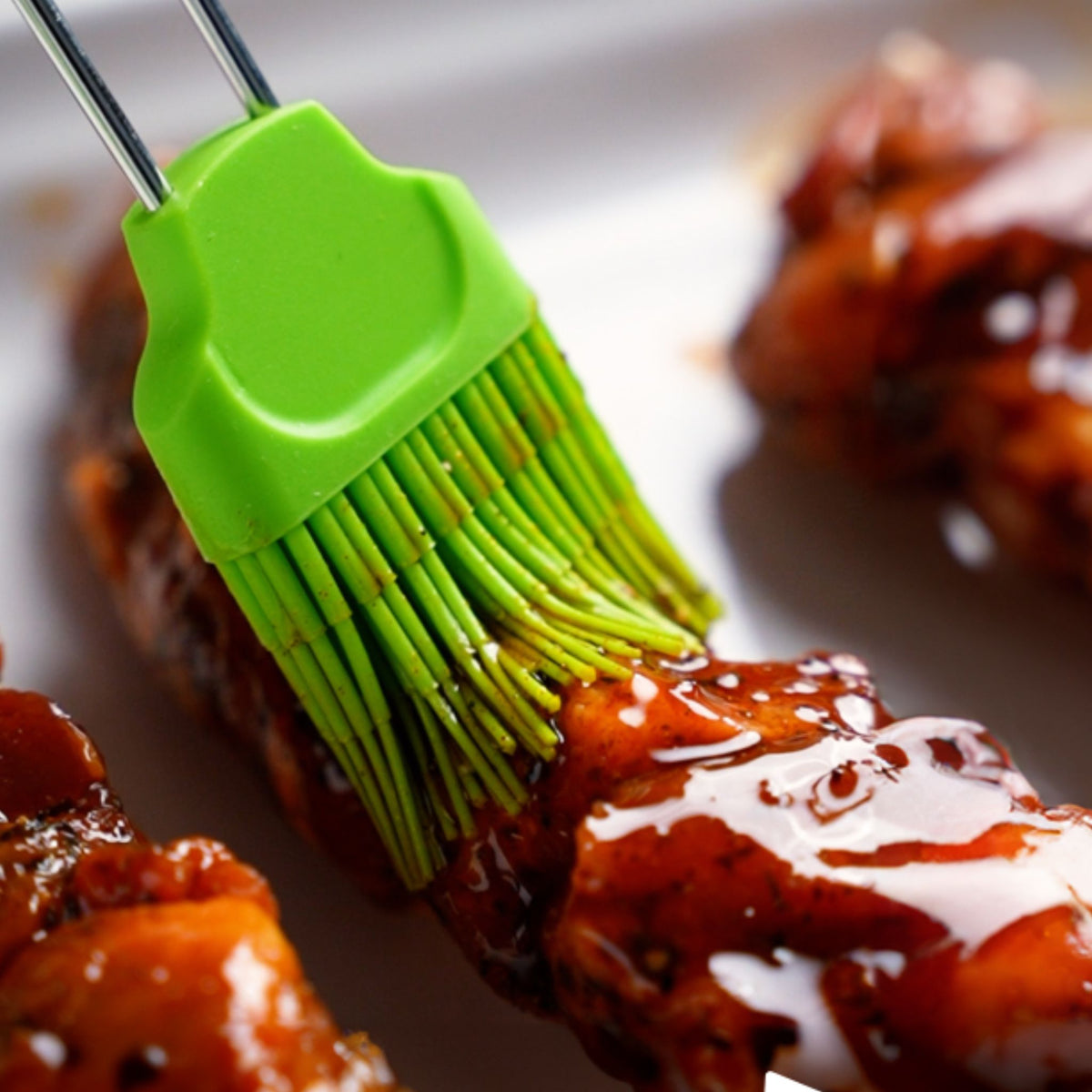 Grüner Silikonpinsel glättet glänzende Barbecue-Sauce auf gegrilltem Fleisch.