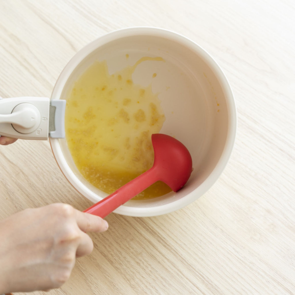Rote Schöpfkelle aus Silikon mit ergonomischem Griff in weiß, in weißem Kochtopf mit Soße.