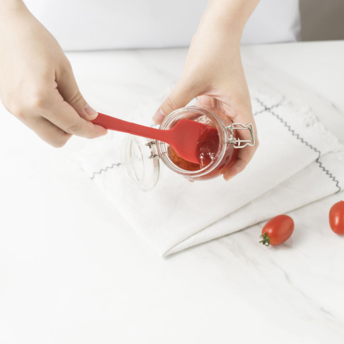 Roter Flexlöffel nimmt Honig aus kleinem Glas auf weißem Untergrund.