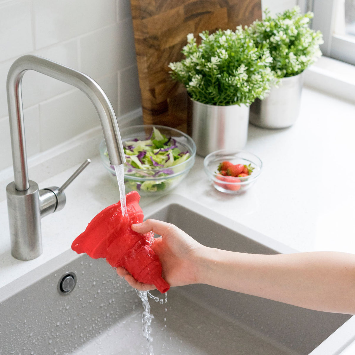 Roter faltbarer Trichter aus flexiblem Silikon, wird unter fließendem Wasser gereinigt.