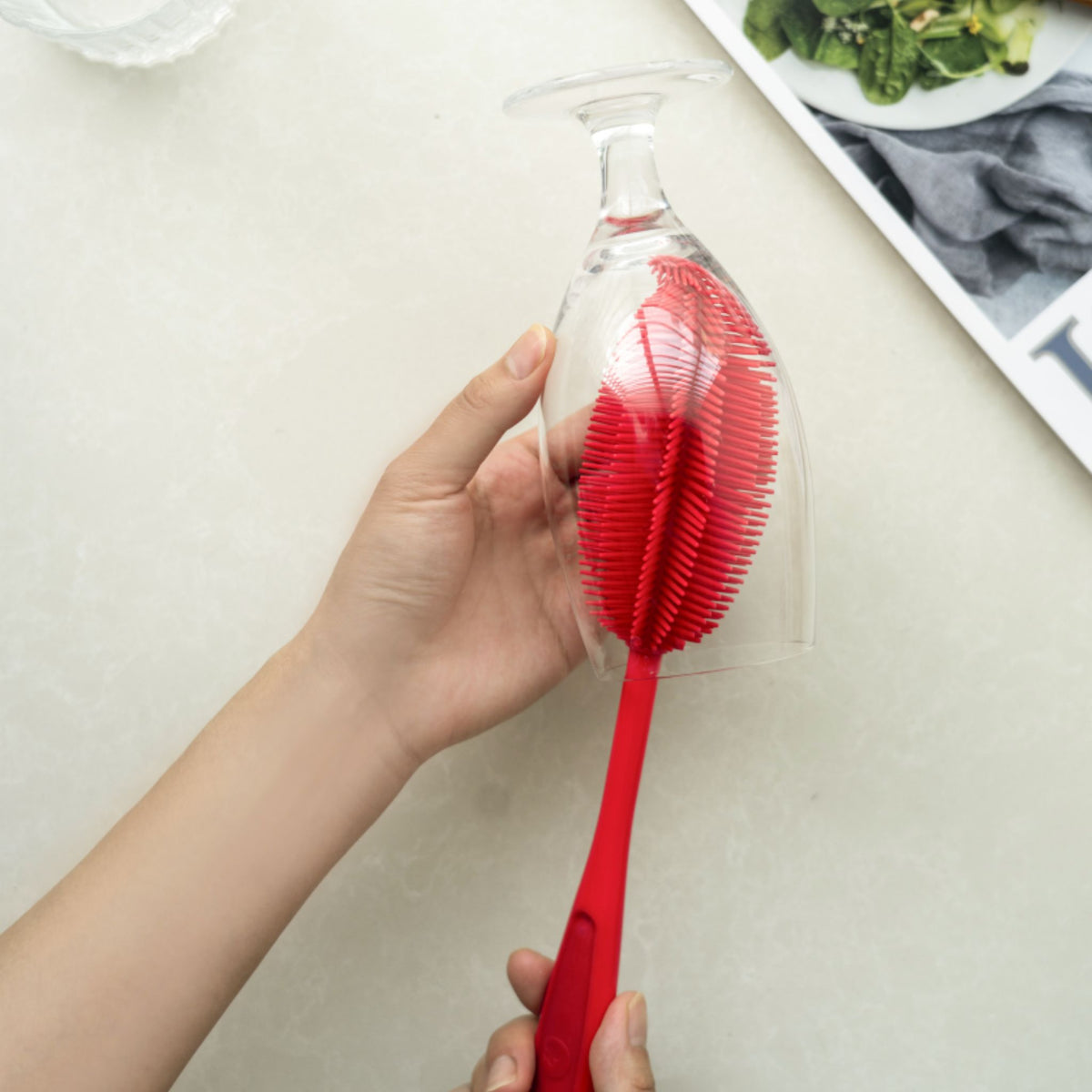 Rote Flaschenbürste mit flexiblem Bürstenkopf, handgehalten in einem Glas.