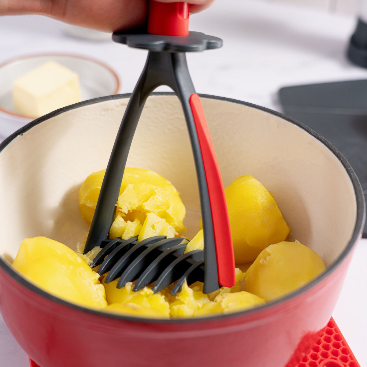 Roter Kartoffelstampfer zerdrückt gekochte Kartoffeln in rotem Topf aus Emaille.