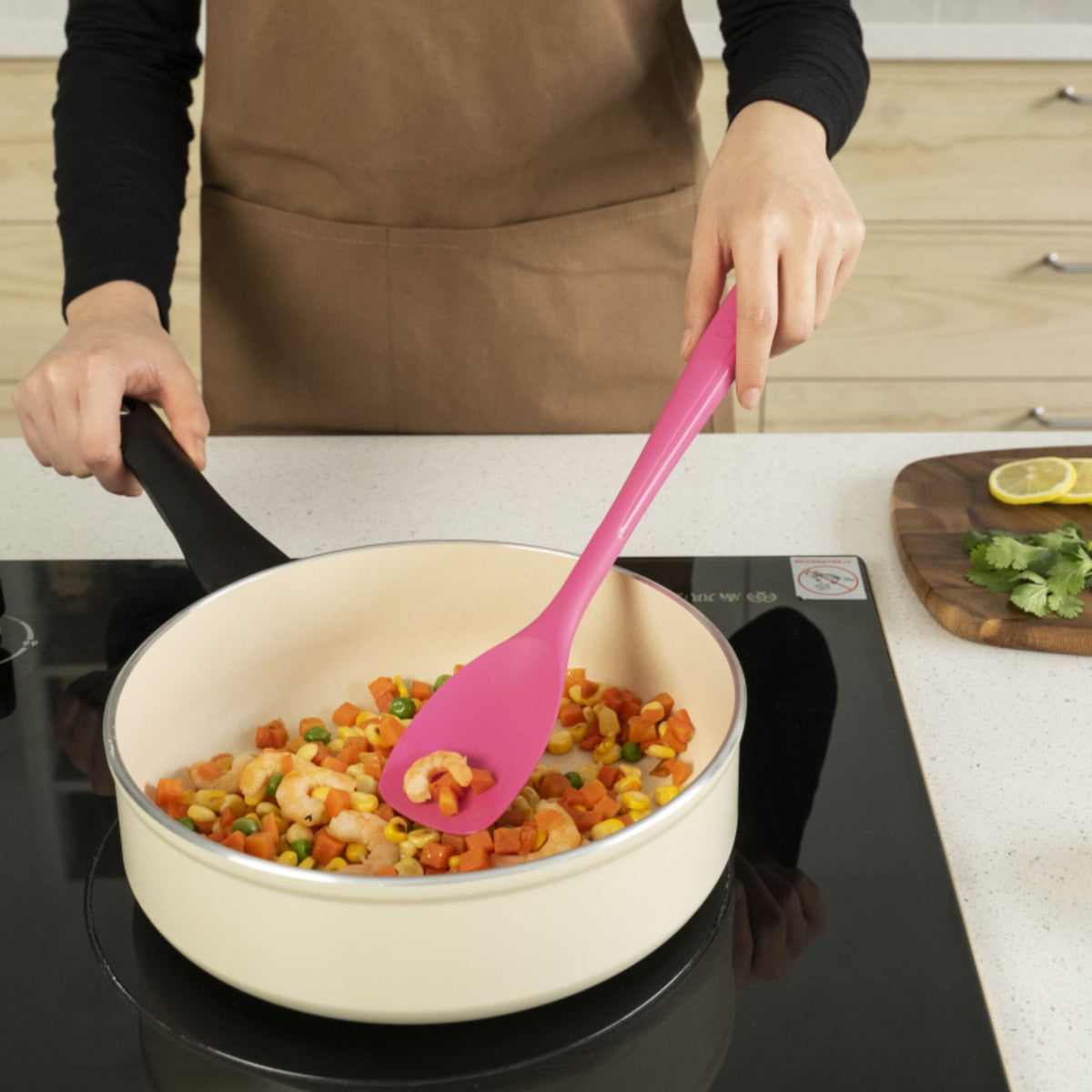 Anthrazitfarbene Pfanne mit Gemüse und flexibler pinker Silikonlöffel beim Rühren.