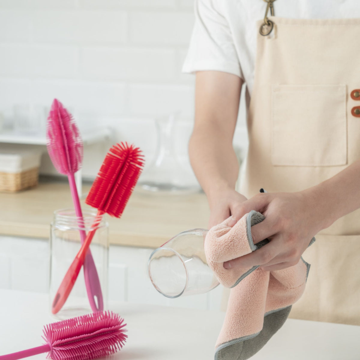 Hand hält altrosa Geschirrtuch und wischt Glas in moderner Küche.