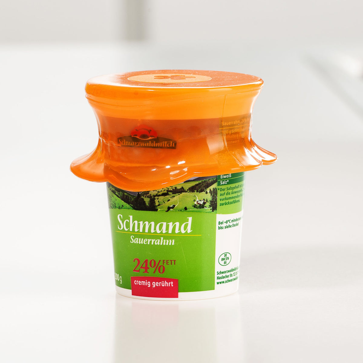 Grüner Schmand-Becher mit orangefarbenem Kunststoffdeckel und 5,5 cm Durchmesser.