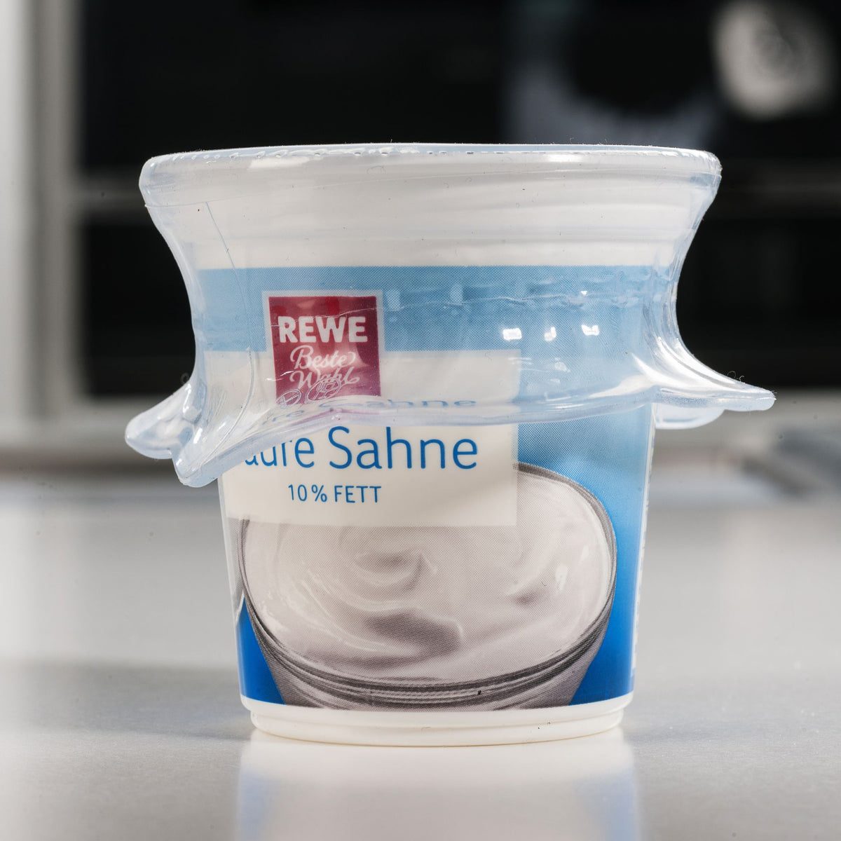 Becher mit blauer Sahnepackung und 10% Fettgehalt auf weißem Hintergrund.