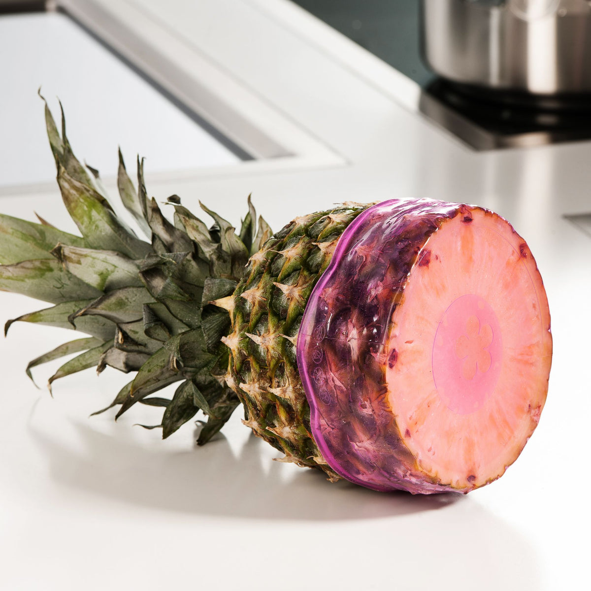 Ananas mit grünen Blättern und einer farblich veränderten, pink-violetten Schnittfläche auf weißer Arbeitsfläche.