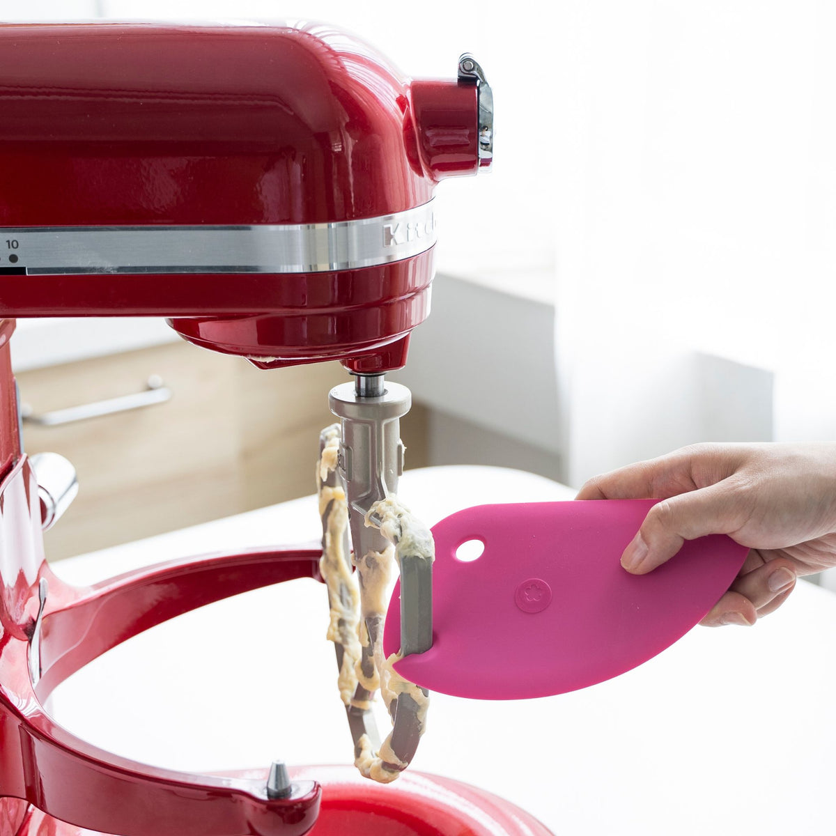 Pinkfarbene flexible Teigkarte aus Silikon am Rührgerät mit Teigrest daran.