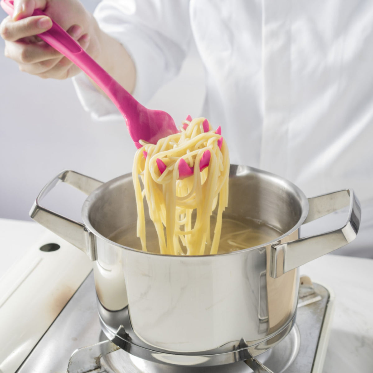 Anthrazitfarbener Pastalöffel hebt Spaghetti aus einem Edelstahltopf.