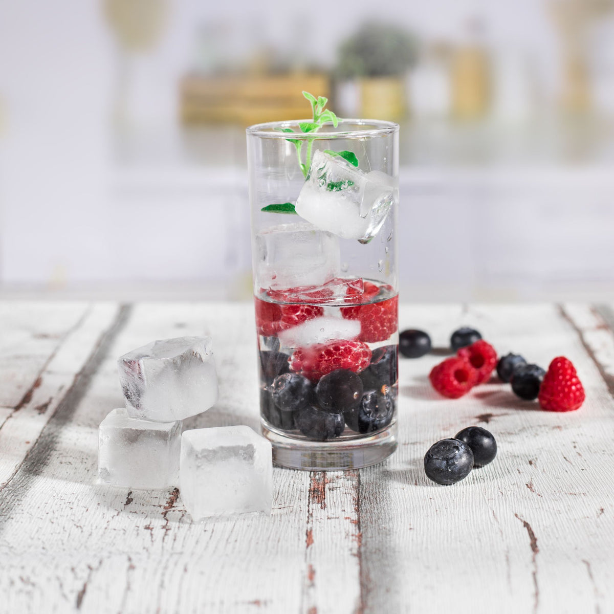 Halbrunde Eiswürfelform mit klaren Eiswürfeln in klarem Glas mit Beeren auf Holztisch.
